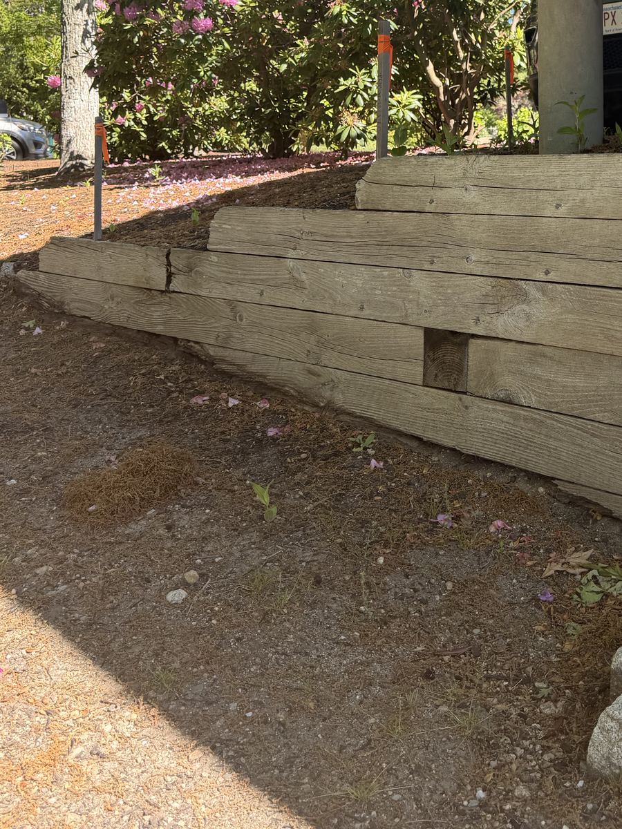 Before — stacked timber sleepers leaning out of line, split along the grain and rotted at the ends