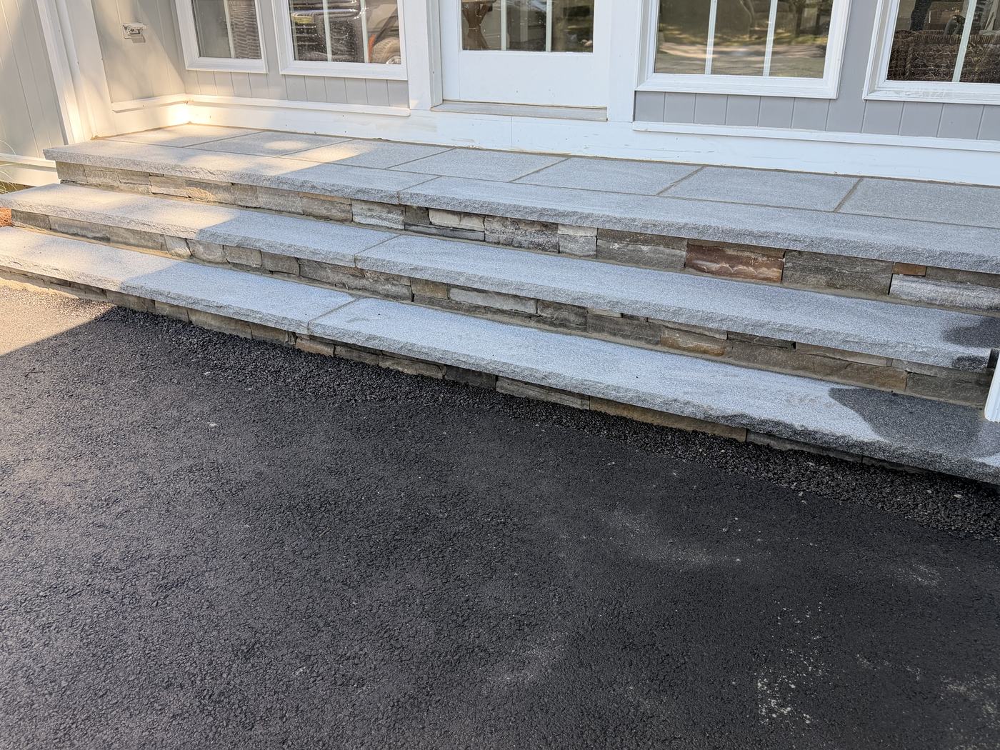Three granite steps running the full width of the doors, risers faced in laid stone, landing on matched granite above