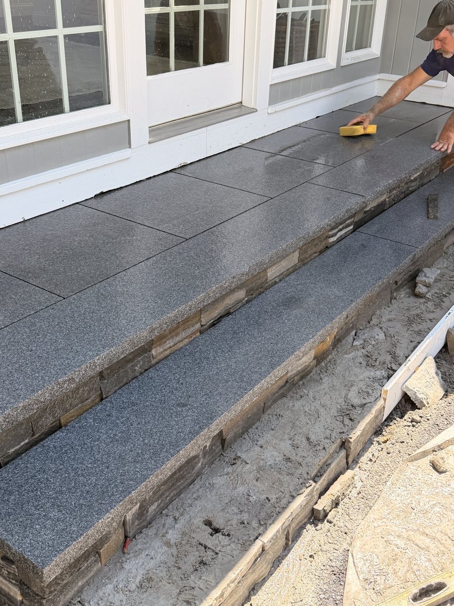 Mid-build, the far half of the run still open with mortar and stone chips, joints being sponged off by hand