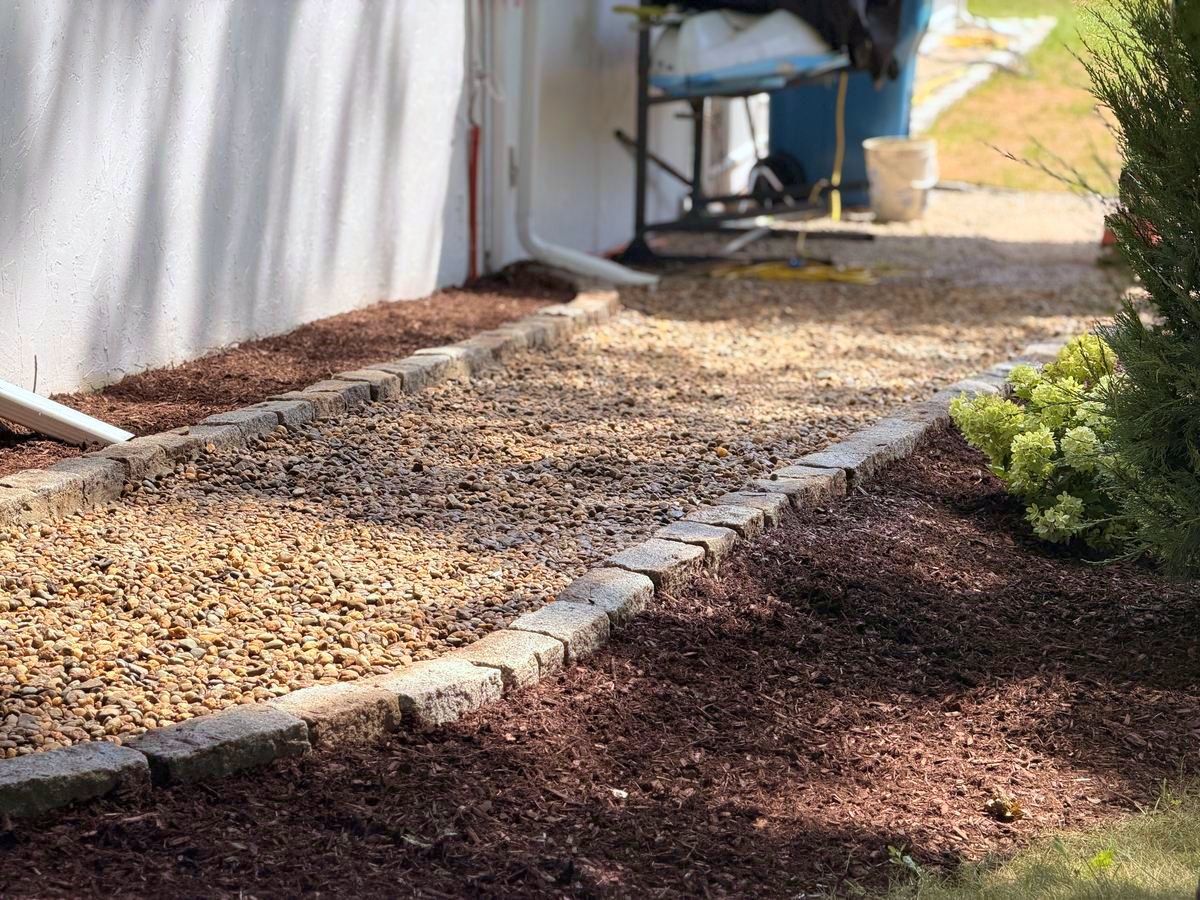 Cobble-edged stone strip along the foundation, mulched beds either side
