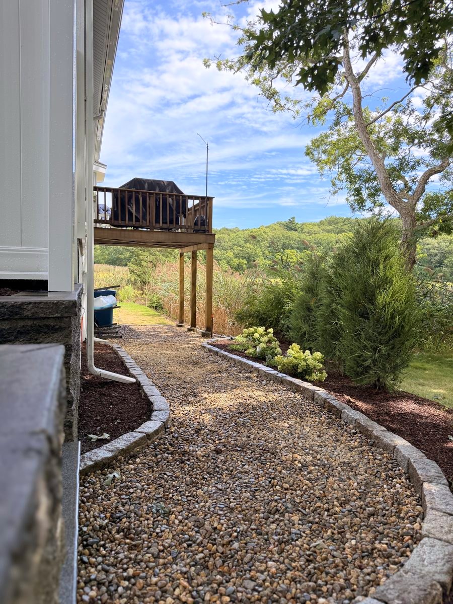 Cobble-edged stone walk curving along the side of the house toward the deck, planted bed alongside