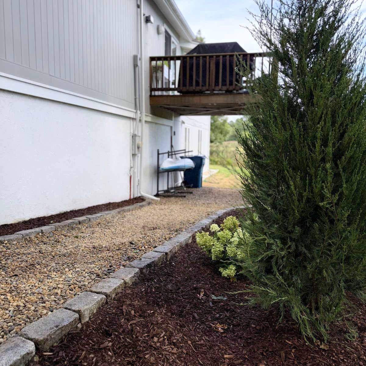 Cobble edge holding the bed line, stone run carrying past the foundation to the deck