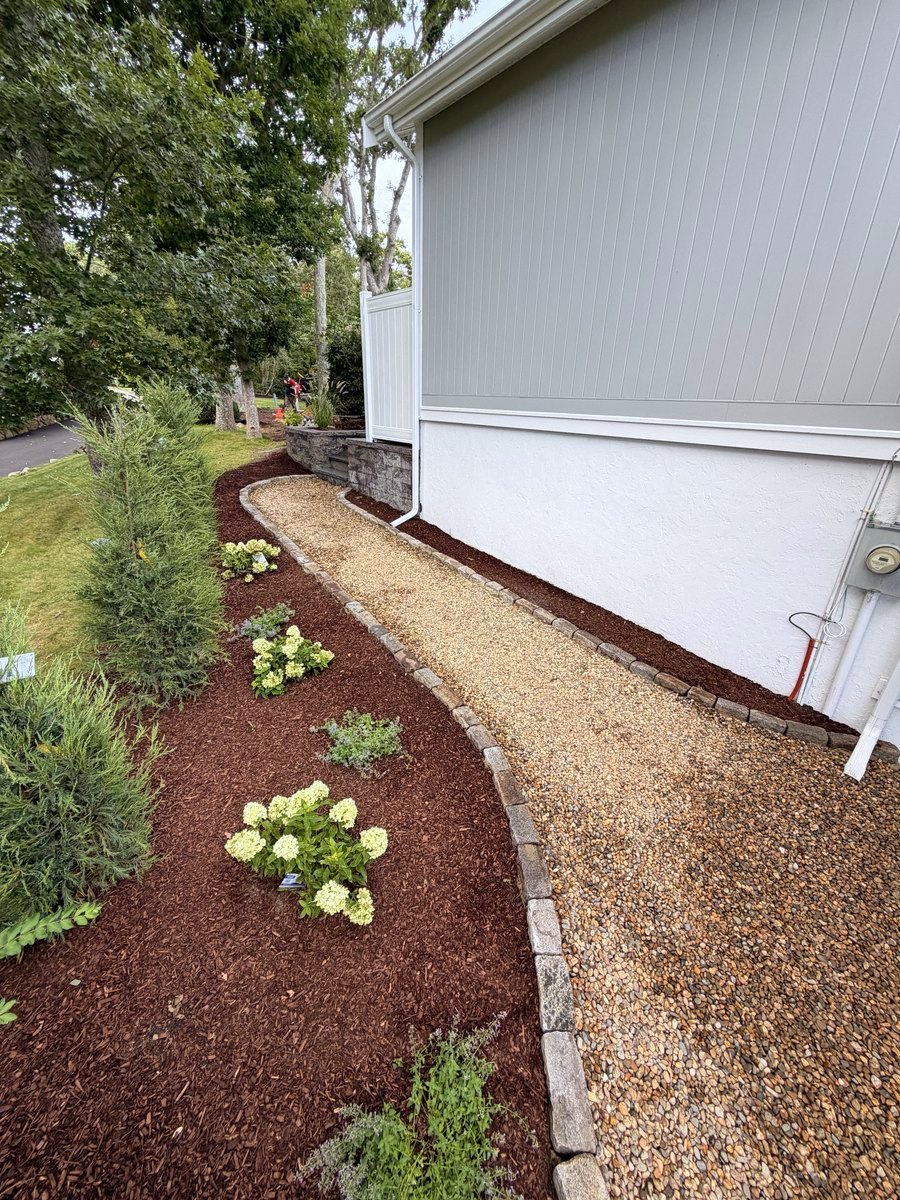 The washed stone run held between cobble and mulch, hydrangeas planted out along the bed