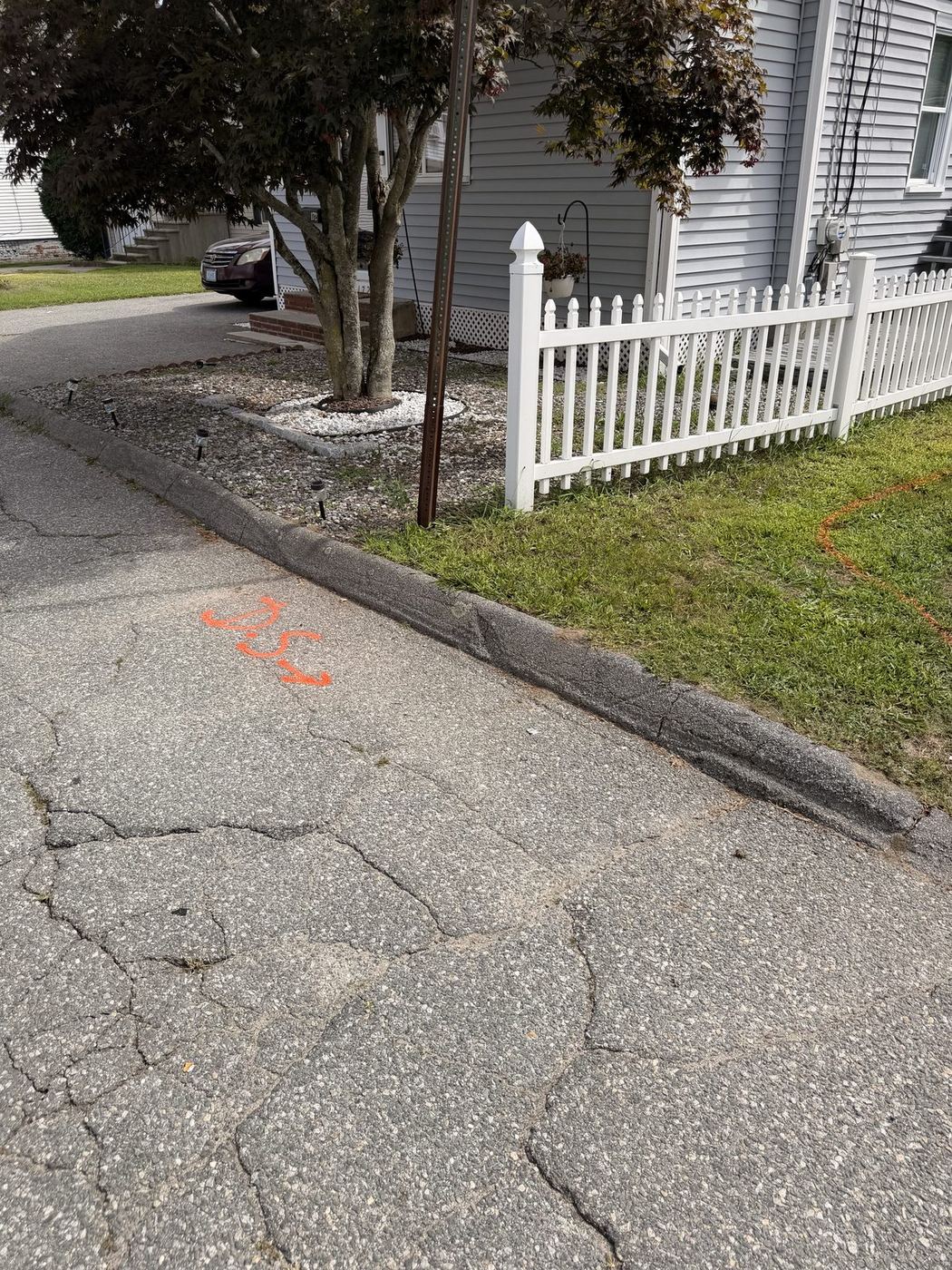 The old curb cut and cracked apron at the street, marked for the new driveway
